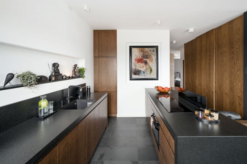 Niskie szafki kuchenne zapewniają sporo miejsca do przechowywania. W głębi, w specjalnie do tego przygotowanej wnęce umieszczono lodówkę w zabudowie. Fronty wykonano z ciemnego forniru, a blaty ze szczotkowanego granitu Indian Black Dark. Wszystkie prace stolarskie w całym mieszkaniu wykonał niezawodny stolarz Krzysztof Gołębiewski. A prace wykończeniowe ekipa, którą szczególnie, bo po 15 latach współpracy, ceni sobie projektantka. Jej szefem jest Piotr Malanowski.