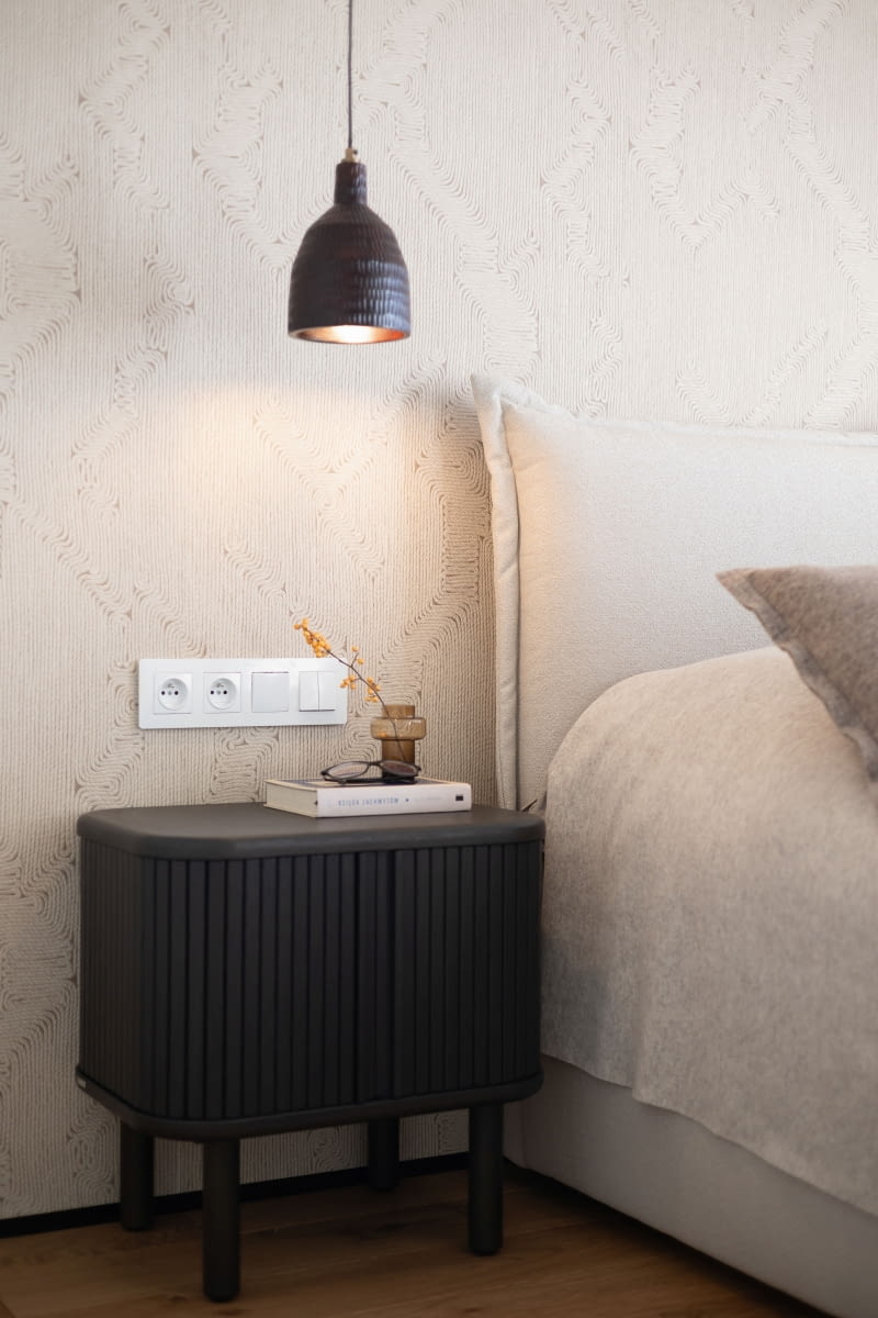 W sypialni styl boho reprezentują też lampy: duży, o średnicy 100 cm, rattanowy klosz Lejek z balibali.pl oraz wiszące po obydwu stronach łóżka, czarne, drewniane lampy z kavehome.com. Do czarnych opraw dobrano z tego samego sklepu szafki nocne w równie ciemnym wykończeniu.