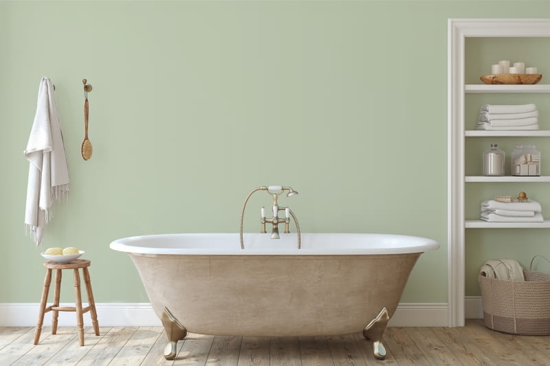 Łazienka w stylu vintage łączy pastelowe barwy z mosiężną armaturą i wolno stojącą wanną na charakterystycznych nóżkach.