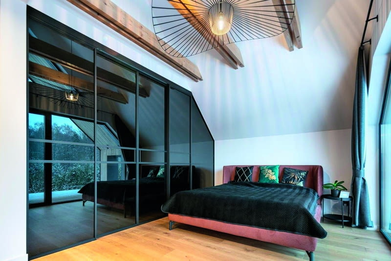 W sypialni gospodarzy, na górnej kondygnacji,  zwracają uwagę m.in. fantazyjny żyrandol oraz  panel roślinny, przypominający podobny motyw  widoczny w salonie. Pomysł nań właściciele  zaczerpnęli z internetu, a dodatkowo pan Paweł  połączył panel z opaską drzwi z wbudowanymi  LED-ami, podświetlającymi kompozycję