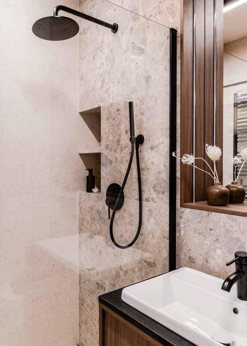 Piękno łazienkowej aranżacji idzie w parze z jej funkcjonalnością. W prysznicu przewidziano wygodne miejsce na kosmetyki, podobnie jak przy lustrze. Nad stelażem WC znalazła się zamykana szafka  z półkami, a w rogu przy wejściu zaprojektowano wysoką zabudowę mieszczącą pralkę i suszarkę.