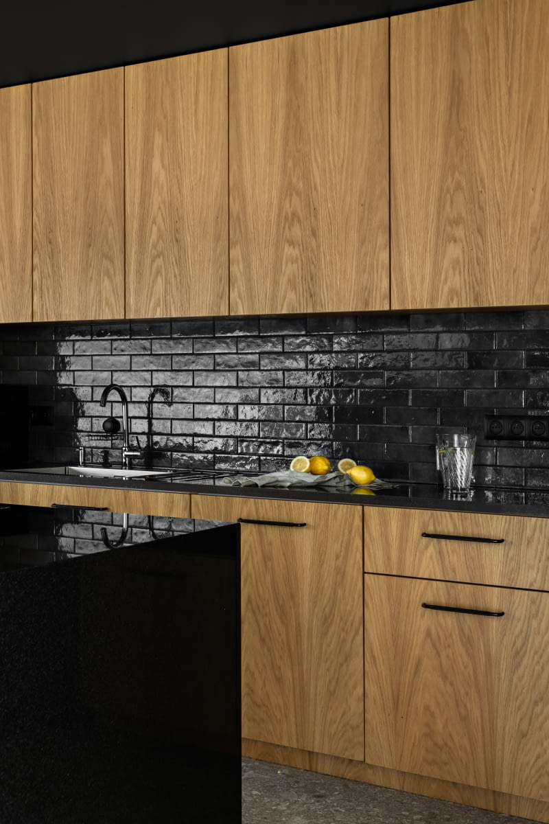 Ścianę nad blatem chronią czarne płytki-cegiełki, pochodzące od tego samego producenta i w tym samym formacie co zielone kafle na obudowie kominka. Powtórzenie tego motywu na murku między kuchnią a jadalnią harmonijnie spaja wystrój całego otwartego wnętrza parteru. Ścianę nad blatem chronią czarne płytki-cegiełki, pochodzące od tego samego producenta i w tym samym formacie co zielone kafle na obudowie kominka. Powtórzenie tego motywu na murku między kuchnią a jadalnią harmonijnie spaja wystrój całego otwartego wnętrza parteru.