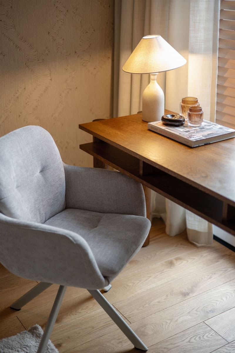 Przy jednym z okien urządzono niewielki kącik do pracy z dębowym biurkiem Bold marki Tamo oraz obrotowym krzesłem tapicerowanym beżowoszarą tkaniną.