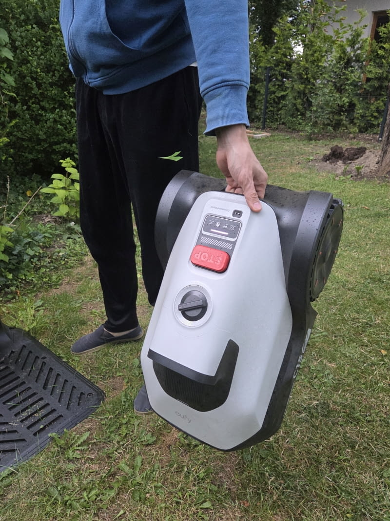 Robot jest stosunkowo lekki i wygodny do przenoszenia — uchwyt na górze obudowy ułatwia przemieszczanie między strefami ogrodu. Eufy C15 podniesiony — stacja bazowa i spód robota. Robot jest stosunkowo lekki i wygodny do przenoszenia — uchwyt na górze obudowy ułatwia przemieszczanie między strefami ogrodu.