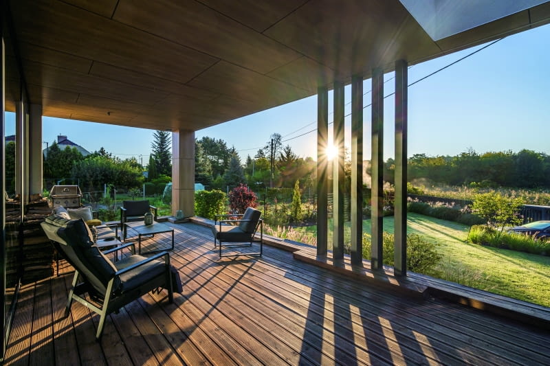 Pięć zgeometryzowanych słupków tworzy przesłonę do ciekawej gry słonecznego światłocienia. W tej części tarasu w ciepłe miesiące „działa” dodatkowy salon-kuchnia, czyli rekreacyjna  przestrzeń zadaszona oraz wyposażona w wygodne meble i stacjonarny grill