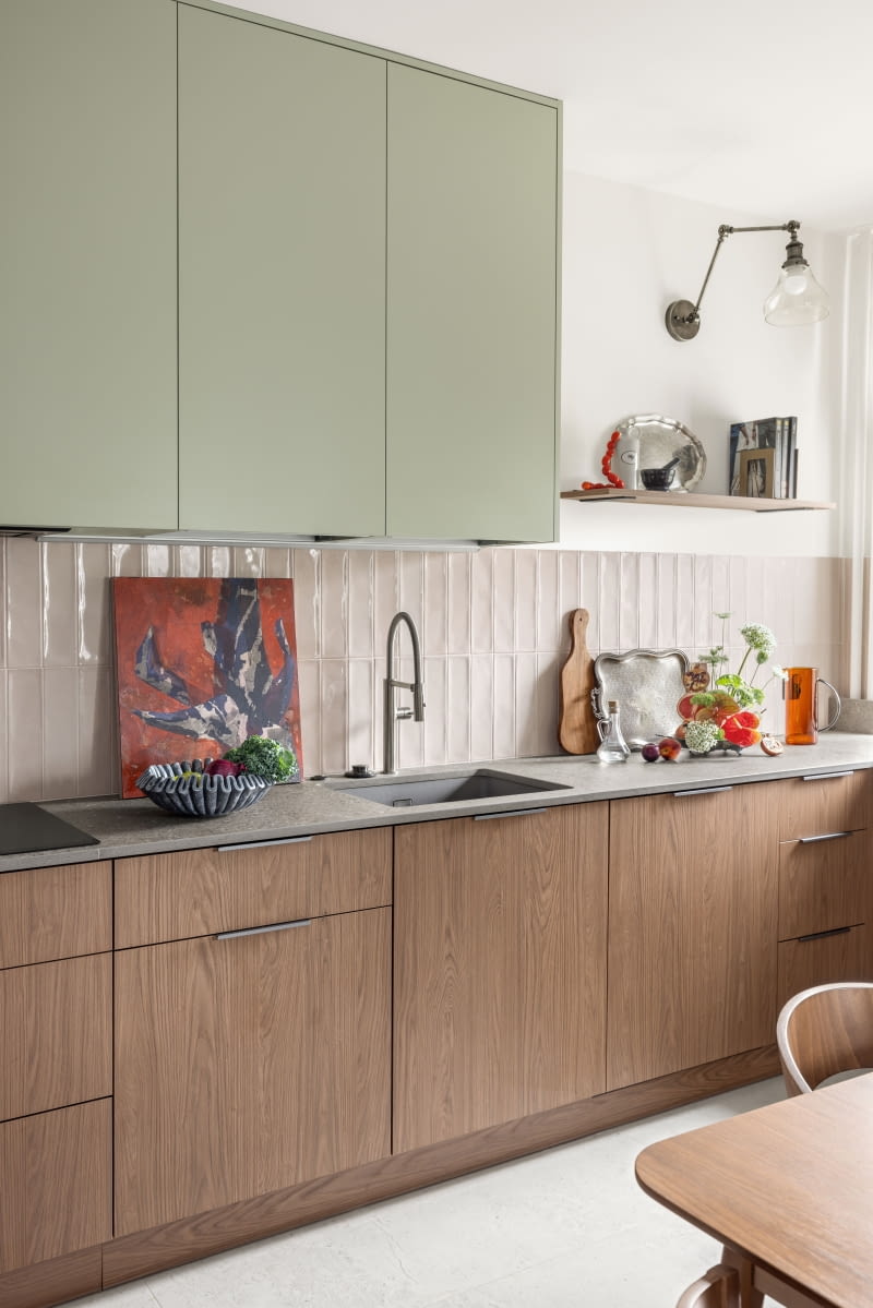 Szafki kuchenne wykonano z płyt laminowanych marki Egger. Na blaty wybrano spiek kwarcowy ze wzorem kamienia od Neolith. Jego szarość idealnie uzupełnia kolorystyczną kompozycję szałwiowych i drewnianych frontów szafek oraz beżowych płytek na ścianach. Obraz z czerwonym tłem to kolejne dzieło Oli Munzar z cyklu „Plant Porn 12”. Pozostałe obrazy w mieszkaniu pochodzą z serii „Brzuch i Reszta” tej artystki. Szafki kuchenne wykonano z płyt laminowanych marki Egger. Na blaty wybrano spiek kwarcowy ze wzorem kamienia od Neolith. Jego szarość idealnie uzupełnia kolorystyczną kompozycję szałwiowych i drewnianych frontów szafek oraz beżowych płytek na ścianach. Obraz z czerwonym tłem to kolejne dzieło Oli Munzar z cyklu „Plant Porn 12”. Pozostałe obrazy w mieszkaniu pochodzą z serii „Brzuch i Reszta” tej artystki.