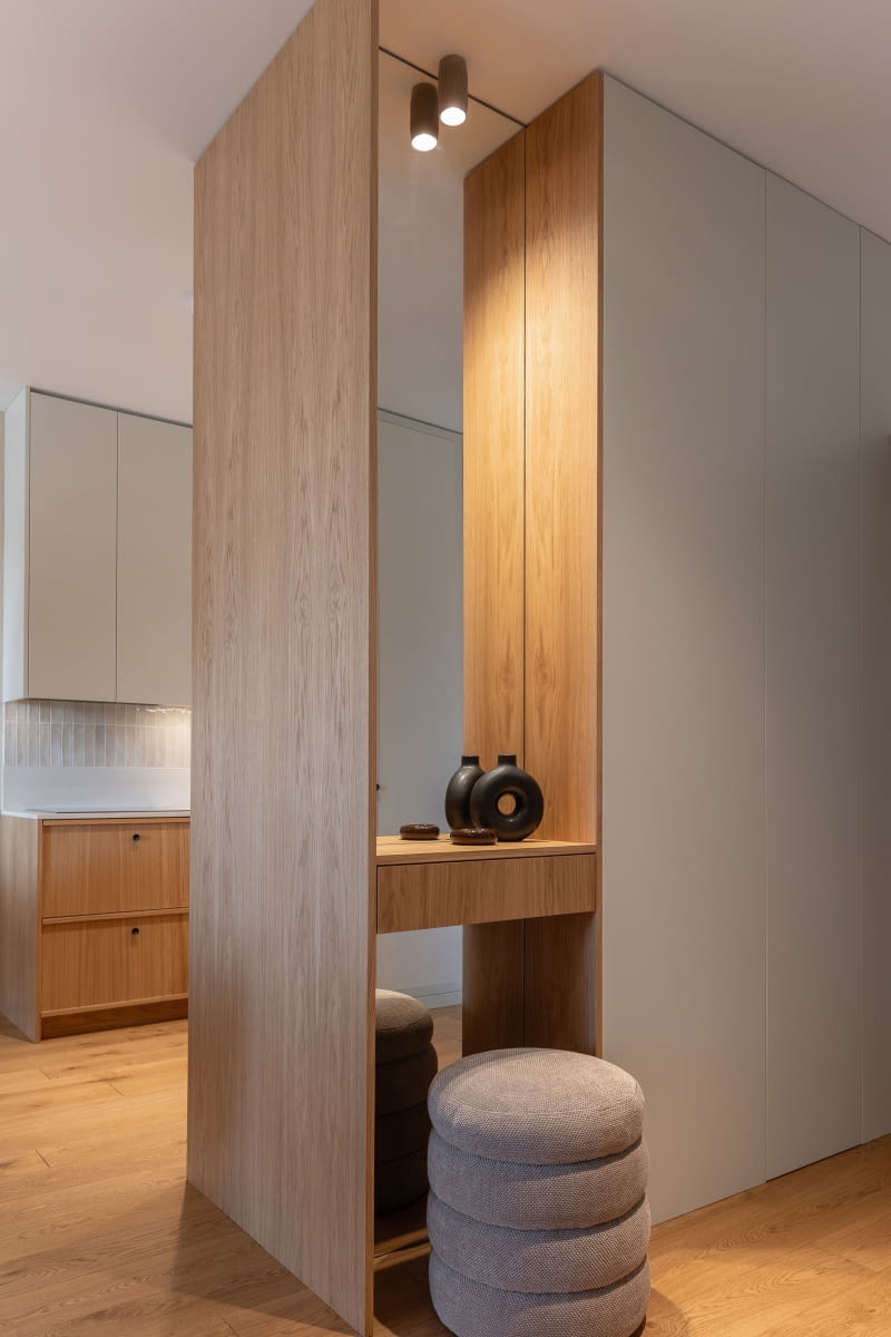 Tył modułu z lodówką od strony holu wykończono lustrem. Taflę przecina prosta szuflada pełniąca funkcję  przydatnej, podręcznej półki przy wejściu, a delikatnie podświetlenie wnęki ułatwia przeglądanie się w lustrze.  W całym mieszkaniu – poza łazienką – ułożono dębowe, olejowane deski z kolekcji Art firmy Mat-Tar, które wprowadzają do wnętrza naturalne ciepło i jednolity charakter.