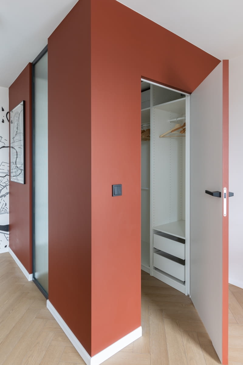 Wybudowana w sypialni garderoba została wyposażona w zabudowę do przechowywania z systemu Pax marki Ikea. Wnętrze dodatkowo doświetla przeszklenie ściany od strony klatki schodowej, wykonane na zamówienie ze szkła ESG Master Ligne. Pionowe ryfle przeszklenia nawiązują do innych wertykalnych linii w aranżacji mieszkania.