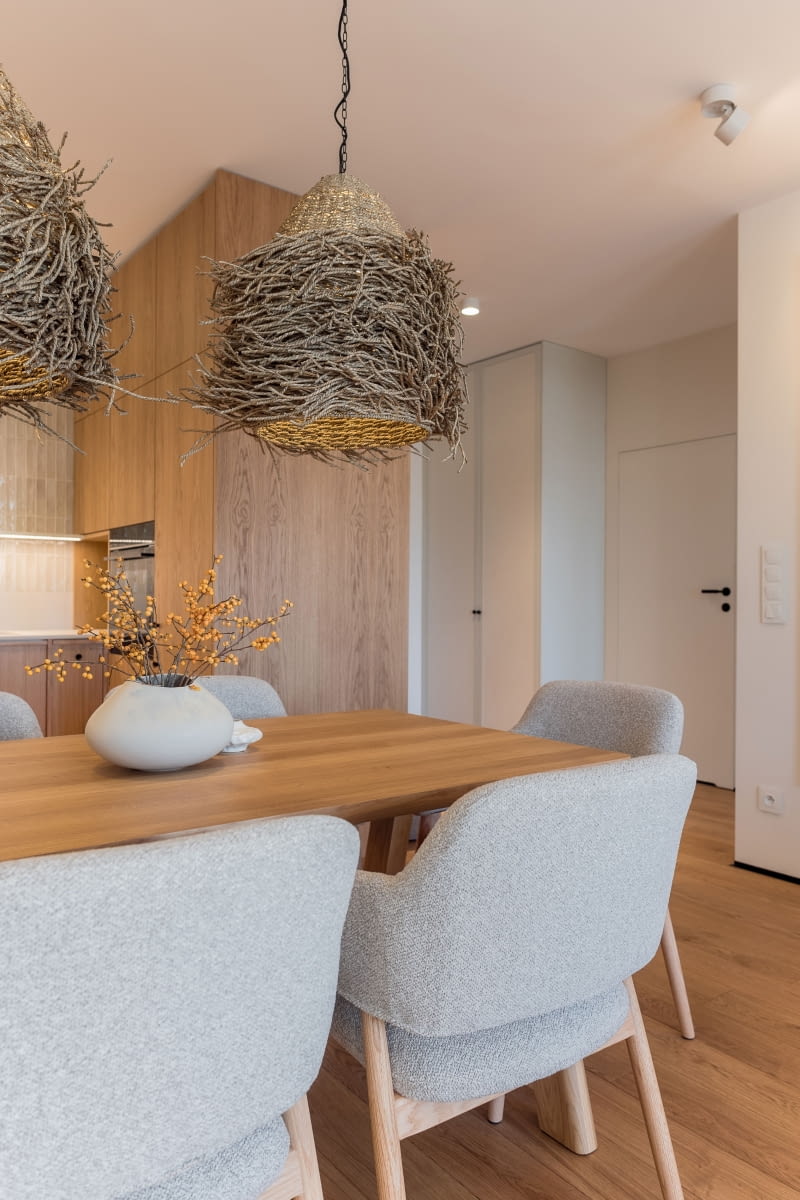 Narożny moduł zabudowy kuchennej, z ukrytą w nim lodówką do zabudowy, wykończono dębowym fornirem z trzech stron – od strony kuchni, jadalni i holu – tworząc spójną, elegancką bryłę widoczną w całej strefie dziennej. Na drugim planie zdjęcia, w holu – szafa z frontami wykończonymi tapetą à la płótno.