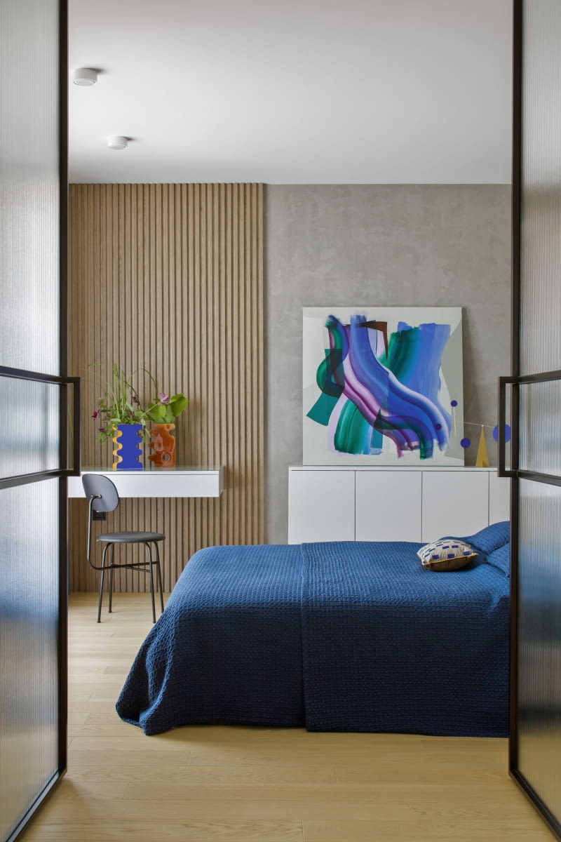 Widoczną z salonu ścianę w sypialni rodziców wykończono drewnopodobnymi panelami i tynkiem naśladującym beton. Stały się tłem dla białego biurka do pracy i szafki oraz ustawionych na nich dekoracji: obrazu Doroty Pawiłowskiej, wazonów Pani Jurek czy ruchomej rzeźby Volta Mobiles z NAP. Przy toaletce stanęło upolowane w outlecie meblowym piękne krzesło Audo Copenhagen Afteroom.