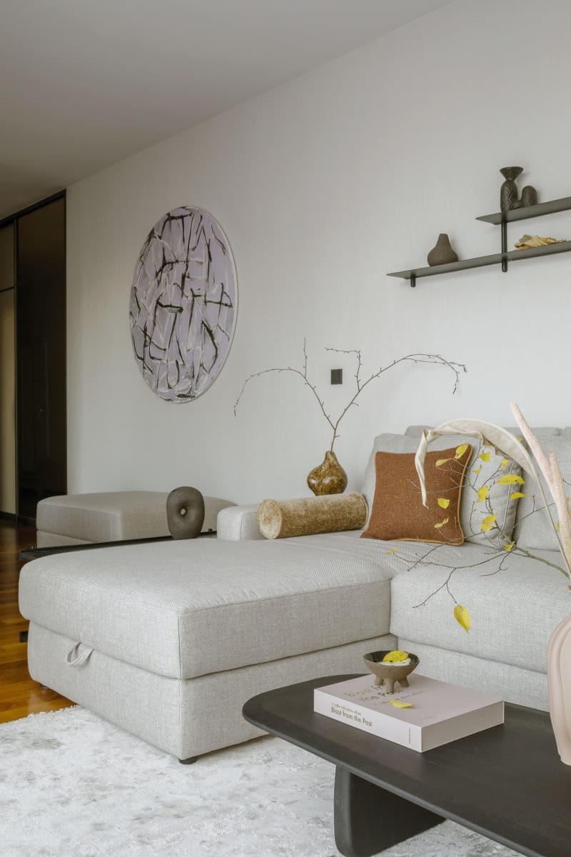 Wyposażenie salonu składa się z komfortowego, beżowego narożnika marki Gala Collezione,  a dalej czarnego, drewnianego stolika kawowego i szafki RTV z Kave Home, a także niskiej, czarnej, metalowej konsoli i wiszącej na ścianie półki  – obydwie ze sklepu Westwing.