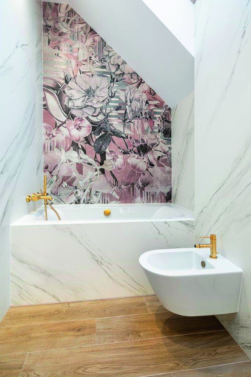 W dziecięcej łazience ulokowanej niedaleko sypialni córek również zadbano o łagodny charakter aranżacji przestrzeni, wypełnionej spokojnymi  barwami, nieco baśniowymi oraz florystycznymi elementami i przyjazną armaturą. Na podłodze, podobnie jak w prawie całym domu, solidny  kawałek natury w postaci drewnianych paneli