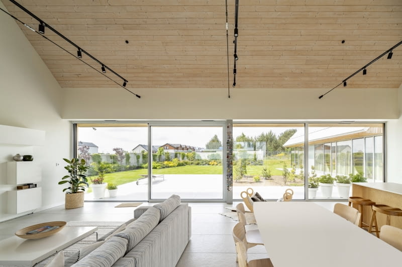 Sercem wnętrz budynku jest otwarta część dzienna. To połączona ze sobą przestrzeń kuchni, jadalni i salonu. Uzupełnienie stanowi wszystko to, co dzieje się za szerokim pasem okien, rozciągniętym niczym ekran