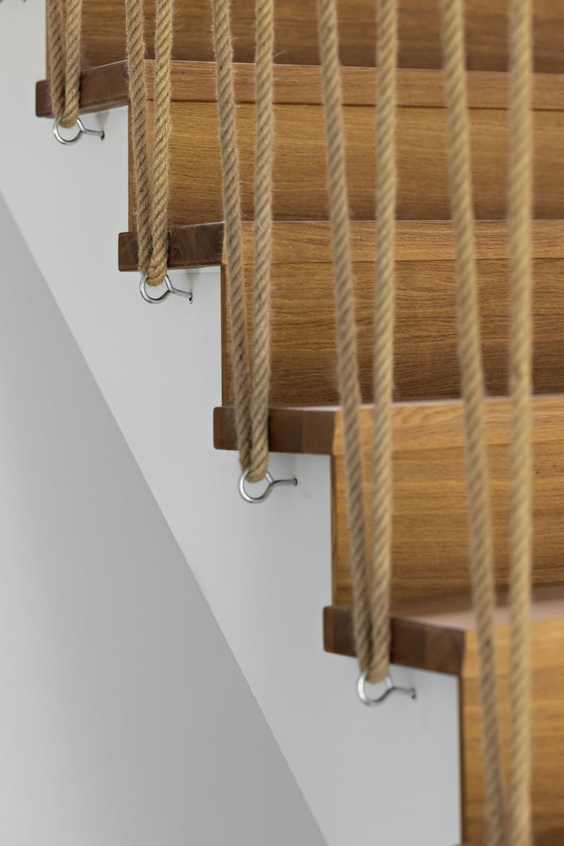 Betonowe schody prowadzące na piętro wykończono drewnem, a ich oryginalnym uzupełnieniem jest barierka z jutowych lin – pomysł i własnoręczna realizacja pana domu. Dla wygody zamontowano także tradycyjną poręcz biegnącą wzdłuż ściany. Betonowe schody prowadzące na piętro wykończono drewnem, a ich oryginalnym uzupełnieniem jest barierka z jutowych lin – pomysł i własnoręczna realizacja pana domu. Dla wygody zamontowano także tradycyjną poręcz biegnącą wzdłuż ściany.