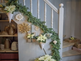 Kremowo-białe poinsecje, zarówno cięte, jak i doniczkowe, zdobią balustradę i prezenty.