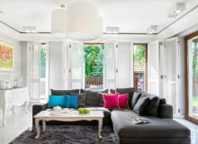 W salonie króluje rozłożysta rozkładana kanapa z szezlongiem - trzeba było wybrać taką, by pomieścili się na niej rodzice i trzy córeczki. Wokół podłogi z dębu bielonego biegnie pas polerowanych płytek gresu, które sprawdzają się szczególnie w okolicy kominka. Chłód szarych ścian i płytek ociepla puszysty dywan w odcieniu antracytu. salon, aranżacja salonu, wystrój wnętrz