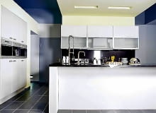 Jedną ścianę zabudowano od podłogi do sufitu. Wbudowany sprzęt tworzy z szafkami idealną płaszczyznę. Zlew i kuchenkę umieszczono w wyspie wysuniętej na środek pomieszczenia.