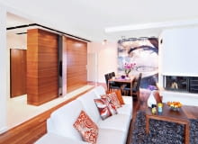 Gospodarze, którzy lubią przestronne i jasne wnętrza, zdecydowali się połączyć salon z przedpokojem i kuchnią. Uzyskanej w ten sposób strefy dziennej nie zamierzali zagracać masywnymi wolno stojącymi meblami do przechowywania. Z drugiej strony zdawali sobie sprawę, że są one w domu konieczne. Dylemat rozwiązała projektantka, proponując zbudowanie meblościanki, która oddzieliłaby strefę wypoczynkową od przedpokoju, a jednocześnie zapewniła wygodne schowki. Pojemną szafę, sięgającą od podłogi do sufitu, zrobiono z płyty fornirowanej egzotycznym tekiem (z tego samego drewna jest parkiet).