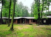 Sytuacja przed przebudową. Widok od frontu na nieproporcjonalnie niską bryłę domu otoczoną wysokimi drzewami Sytuacja przed przebudową. Widok od frontu na nieproporcjonalnie niską bryłę domu otoczoną wysokimi drzewami