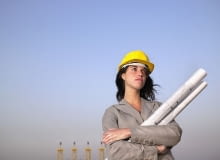 architektka Woman in hard hat holding drafts with towers in background --- Image by cultura/Corbis