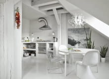 Biała podłoga z żywicy, pomalowane na biało ściany, dębowe belki i słupy. Wszystko to sprawia, że wysokie wnętrze ze skosami wydaje się jeszcze przestronniejsze. Mebli tu niewiele, ale za to głównie klasyki designu. <BR /> MIESZKANIE. Zamiast szafek w kuchni jest murowana zabudowa, która podkreśla surowy klimat wnętrza. Blat i fragmenty ścian wykończono niewielkimi płytkami ceramicznymi. Wokół stołu z tworzywa sztucznego stoją designerskie krzesła. Tak zwany druciak zaprojektował w latach 50. XX wieku Harry Bertoia, pantony z tworzywa sztucznego to dzieło Vernera Pantona (lata 60.). Stół oświetla dekoracyjna lampa z tworzywa sztucznego i kryształków. Obraz 'Wypadek', wiszący na ścianie pod skosem dachu, namalowała Agnieszka Kieliszczyk. wystrój wnętrz, styl loftowy, aranżacje wnętrz