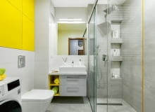 Wnękowe półki w kabinie prysznicowej celowo rozmieszczono na różnej wysokości - dzięki temu mogą z nich wygodnie korzystać i duzi, i mali. Warto dodać, że takie półki są bezpieczne i dla domowników (nie uderzą się o wystające elementy), i dla ustawionych na nich kosmetyków (nie spadną na podłogę). Na podłodze położono gresowe płytki Timbre Grey, na ścianach - Timbre White i Timbre cement; przy kabinie wkomponowano szklaną listwę Yellow (wszystko z firmy Tubądzin).
