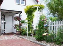 Przy domu w sezonie bujnie rosną kwiaty. Obrośnięta pnączami pergola to wejście do przydomowego ogródka. Przy domu w sezonie bujnie rosną kwiaty. Obrośnięta pnączami pergola to wejście do przydomowego ogródka.