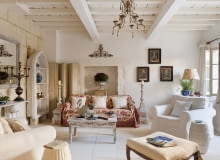 Stone floored provencal sitting room with armchairs, floral sofa throw and distressed wooden coffee table SLOWA KLUCZOWE: provence france french provencal inside indoors day nobody interior design home living room drawing room sitting room sofa floral pattern cream colour artwork seating area animal likeness swan bird shelves shelving tiled floor painted furniture shabby chic white white colour armchair country style horizontal image colour image