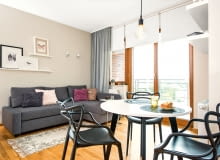 Jedną ze ścian pokoju niemal w całości zajmują przeszklone dwuskrzydłowe drzwi i okno balkonowe. Panoramę okolicy można więc oglądać, nie wstając z kanapy. Zasłona w rogu pełni jedynie funkcję dekoracji, dlatego zawieszono ja na krótkim karniszu. małe mieszkanie, salon, aranżacja salonu