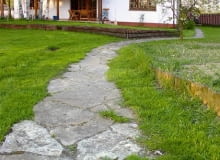 Ścieżka z łamanych płyt kamiennych. Przestrzenie między poszczególnymi płytami są zasypane piaskiem i zarośnięte kępkami traw. DO JEDNORAZOWEJ PUBLIKACJI