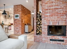 Salon z kominkiem. Cegłą obłożono także drugą ścianę, oddzielającą salon od schodów. Kryje się w niej kominek. W powstałej wnęce składowane są drewniane polana. Od strony korytarza specjalnie zamontowano w niej taflę szkła, żeby było je widać już od wejścia. Widok ten wita gości domu, budując klimat przytulnego, sielskiego zacisza. Dom pod Wrocławiem - połączenie minimalistycznego designu i sielskiego klimatu