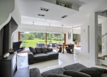 Przed nadmiernym nasłonecznieniem wnętrza w najcieplejsze miesiące roku chronią gładkie podciągane zasłony. Gospodarze podkreślają, że w domu nigdy nie jest za gorąco - prawdopodobnie również dzięki mikroklimatowi stwarzanemu przez sąsiadujący z posesją las. Zimą natomiast trudno przecenić zalety dobrego doświetlenia wnętrz salon, duże okna, koza