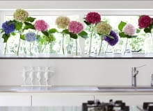 Małe, szklane wazoniki ustawione w rzędzie na parapecie, a w nich duże, pojedyncze kwiaty kolorowych hortensji. Idealna wiosenna aranżacja. kwiaty, aranżacje kwiatowe