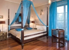 Aranżacje. W tej sypialni bezsprzecznie króluje łóżko o bogatej formie. Mebel z litego drewna ma w rogach wysokie słupki, na których można rozwiesić moskitierę albo baldachim. Tutaj sznurkowe zasłony zamocowano do... lampy sufitowej, a na słupkach zawiązano tylko dolne końce tkanin. Tak "ubrana" lampa daje miłe rozproszone światło. WNETRZA , POKOJ , SYPIALNIA - LOZKO Z NIEBIESKIM BALDACHIMEM , KRZESLO , NIEBIESKIE ZASLONY