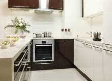 Fiolet i brąz, ulubione barwy pani domu, na jej życzenie grają wiodącą rolę w wystroju wnętrza. Projektantka wybrała ciepły kolor czekolady i dodała kilka różnych odcieni fioletu. W efekcie powstała smakowita, a przy tym bardzo elegancka mieszanka. <BR> MIESZKANIE. W kuchni przeważa odcień białej czekolady. Ściany nad blatem z kompozytu zostały zabezpieczone taflą szkła lacobel w tym samym kolorze. Na podłodze ułożono płyty polerowanego gresu. kuchnia, meble kuchenne, aranżacja małej kuchni