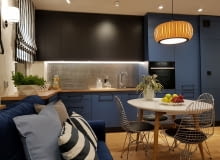 Granatowa zabudowa kuchenna wyglądem bardziej przypomina meble salonowe niż kuchenne. Harmonijnie wpisuje się w aranżację całego pokoju dziennego – poprzez użycie wspólnych kolorów i materiałów, takich jak barwy granatu, czerni i drewna. Kuchnia otwarta na salon. Krzysztof Miruć