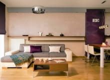 Ściana w salonie, przedzielona na pół długą półką, została wykończona na dwa sposoby - na dole pomalowano ją jasną farbą, na górze położono tynk strukturalny (Fox Dekorator). Aneks wypoczynkowy (z kanapą z Agata Meble) oświetlają halogeny zainstalowane w pasie podwieszonego sufitu oraz lampa (Maxlight); kąt jadalny (ze stołem z firmy Drewnogal) - kinkiety i lampa (Italux). Stolik kawowy to projekt Mileny Maciak. aranżacja salonu, ściana w salonie