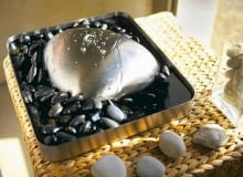 Fontanna domowa. Woda wypływa z czubka stalowej bryły wprost na okalające ją kamyki. Projekt marki Blomus, wys. 8 cm, szer. 32 x 28 cm. Cena: ok. 950 zł, www.fabrykaform.pl Fontanna domowa.