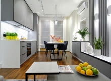 W wąskim salonie trzeba było zmieścić aneks kuchenny, jadalnię oraz strefę rekreacyjną z kanapą i telewizorem. Naprzeciwko zabudowy kuchennej, po drugiej stronie stołu znajduje się niska zabudowa ciągnąca się wzdłuż całego salonu. Wraz z wiszącym nad nią telewizorem i ozdobnymi, pionowymi lamelkami, stanowi element równoważący zabudowę z mebli kuchennych. Wszystkie zaprojektowane przez architekta meble w tym pokoju, jak również w innych pomieszczeniach, są takie same – z szaro-białego, eleganckiego laminatu. Aranżacja wąskiego salonu z aneksem kuchennym