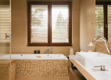 <B> Pojedynczy nie zdziała we wnętrzu wiele, ale w grupie zyskuje moc - ożywia kolorystykę, podkreśla kształt mebli i urządzeń, zdobi. W łazienkach nastał czas mozaiki. </B><BR /> WNĘTRZA: Gospodarze wykończyli mozaiką obudowę wanny oraz ścianę przy umywalce i w kabinie prysznicowej, a więc miejsca najbardziej narażone na kontakt z wodą (wybrano produkt z polerowanego marmuru Emperador włoskiej firmy Sicis). W ten sposób wizualnie podkreślono też strefy mycia i kąpieli. Oprócz mozaiki w łazience zastosowano gres imitujący polerowany trawertyn (płytki 30 x 90 cm i 60 x 90 cm układane na przemian). Odcienie kamienia idealnie pasują do kolorystyki całego wnętrza - na kostkach powtarzają się barwy pozostałych elementów wyposażenia (biel ceramiki, brąz mebli i dodatków, beż gresu). Ciepłe odcienie budują klimat sprzyjający odpoczynkowi. Lustro nad umywalką od góry i od dołu otaczają pasy mozaiki tworzące rodzaj ramy. Do wanny dobudowano schodek wykończony (tak jak cała podłoga) płytami gresu imitującego polerowany trawertyn. W podwieszonym suficie zainstalowano halogeny - dzięki temu można było zrezygnować ze światła sufitowego o dużej mocy i zawiesić jedynie ozdobną lampkę. <B> Pojedynczy nie zdziała we wnętrzu wiele, ale w grupie zyskuje moc - ożywia kolorystykę, podkreśla kształt mebli i urządzeń, zdobi. W łazienkach nastał czas mozaiki. </B><BR /> WNĘTRZA: Gospodarze wykończyli mozaiką obudowę wanny oraz ścianę przy umywalce i w kabinie prysznicowej, a więc miejsca najbardziej narażone na kontakt z wodą (wybrano produkt z polerowanego marmuru Emperador włoskiej firmy Sicis). W ten sposób wizualnie podkreślono też strefy mycia i kąpieli. Oprócz mozaiki w łazience zastosowano gres imitujący polerowany trawertyn (płytki 30 x 90 cm i 60 x 90 cm układane na przemian). Odcienie kamienia idealnie pasują do kolorystyki całego wnętrza - na kostkach powtarzają się barwy pozostałych elementów wyposażenia (biel ceramiki, brąz mebli i dodatków, beż gresu). Ciepłe odcienie budują klimat sprzyjający odpoczynkowi. Lustro nad umywalką od góry i od dołu otaczają pasy mozaiki tworzące rodzaj ramy. Do wanny dobudowano schodek wykończony (tak jak cała podłoga) płytami gresu imitującego polerowany trawertyn. W podwieszonym suficie zainstalowano halogeny - dzięki temu można było zrezygnować ze światła sufitowego o dużej mocy i zawiesić jedynie ozdobną lampkę.