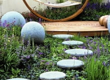 Modern outdoor room has unifying theme of circles and spheres.Concrete balls and stones lead to deck and hammock. Blue ajuga, nepeta and geranium SLOWA KLUCZOWE: Designer Garten Hof Holz H ngematte Kreis Kreise Pflanze Stein Storchschnabel Storchschn bel Trittsteine Wege ausspannen bl´hend enspannen entspannend entspannt erholend friedlich friedvoll geschwungen kreisf^rmig krumm modern relaxed relaxen ruhen zeitgen^ssisch Nicola Stocken Tomkins quadratisch