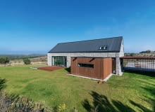 Ten nowoczesny dom nawiązuje bryłą do tradycyjnych wiejskich budynków. Elewację wykończono drewnem i gabionami dom nowoczesny, gabiony, elewacja z gabionów, domy na wsi