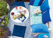 jA summery balcony seen from above with a laid table and aqua coloured cushions on white, outdoor furniture