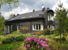 Widok na dom od strony ogrodu. Ciemna elewacja to niecodzienny sposób na wykończenie domu jednorodzinnego. W intensywnie zielonym otoczeniu sprawdza się jednak znakomicie, tworząc piękne tło dla starannie wypielęgnowanych roślin dom na wsi