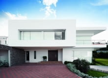 Szeroki nawis piętra skutecznie pełni rolę zadaszenia. Jasne kolory elewacji dodają lekkości całej bryle wejście do domu