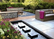 Projekty ogrodów. Gabiony wypełnione kamieniami dobrze izolują różne zakątki ogrodu Small garden with wicker sofas on decked and paved patio, backed by Fargesia murielae - Bamboo hedge. Rectangular pond with row of square water features