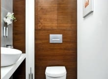 <b> Toaleta powinna być urządzona i wygodnie, i gustownie. Szczególną uwagę warto zwrócić na właściwe oświetlenie i kolorystykę tego niedużego zwykle pomieszczenia. </b> <BR /> TOALETA 1: ŚWIATEŁKO W TUNELU. <BR /> Najciekawszym elementem aranżacji jest tu fornirowana orzechem ściana z podwieszanym sedesem; tą okładziną wykończono zarówno ściankę instalacyjną, jak i fronty zbudowanych nad nią szafek. Ciepły odcień drewna zestawiono z chłodnym szarym gresem położonym na ścianie przy lustrze (pozostałe pomalowano wodoodporną farbą). Pomieszczenie jest utrzymane w stonowanych barwach - bieli, brązach, beżach i szarościach. Oświetlenie zainstalowano w przesmyku między dwiema częściami sufitu podwieszanego. Po zapaleniu światła wąska wnęka, w której stoi szczotka, wygląda bardzo dekoracyjnie.