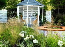 Jednolita ściana trejaża i altany mogłaby sprawiać wrażenie monotonii - zaradziła temu mgiełka kwiatostanów traw w kolorze starego złota Table and chairs in wooden pavilion, outdoor dining, raised circular pond, Deschampsia cespitosa SLOWA KLUCZOWE: rose flower grasses perennial summerhouse gate pond seating furniture The Sadolin Refresh and Revive Garden RHS Hampton Court Flower Show 2010 Kathryn Hibberd June Summer small town romantic designer horizontal wide shot sunny white