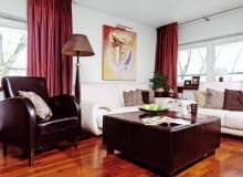 Aranżacje. Kącik wypoczynkowy tonie w brązach i beżach - z tej tonacji wyłamują się tylko zasłony z jedwabnej tafty i obraz wiszący nad kanapą. Na podłodze (podobnie jak w pozostałych pokojach i na antresoli) ułożono drewno merbau w ciepłym odcieniu brązu. W roli stolika kawowego doskonale sprawdza się pokaźny puf obity skórą. UWAGA ! PONOWNA PUBLIKACJA WYLACZNIE ZA ZGODA WLASCICIELI