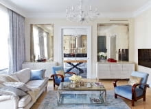 Pod symetrycznymi taflami postarzanych luster (Renes) stoją komody projektu Marii Kowalewskiej pokryte płatkami srebra. Jedna pełni funkcję barku, druga kryje sprzęt audio wideo. Kanapy (MTI Furninova), szklany stolik Cruise (BBHome). W głębi widoczna kuchnia i jadalnia.